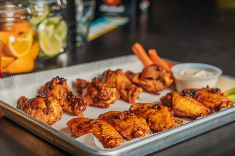 A metal tray of glazed chicken wings with carrots, celery, and ranch dressing.